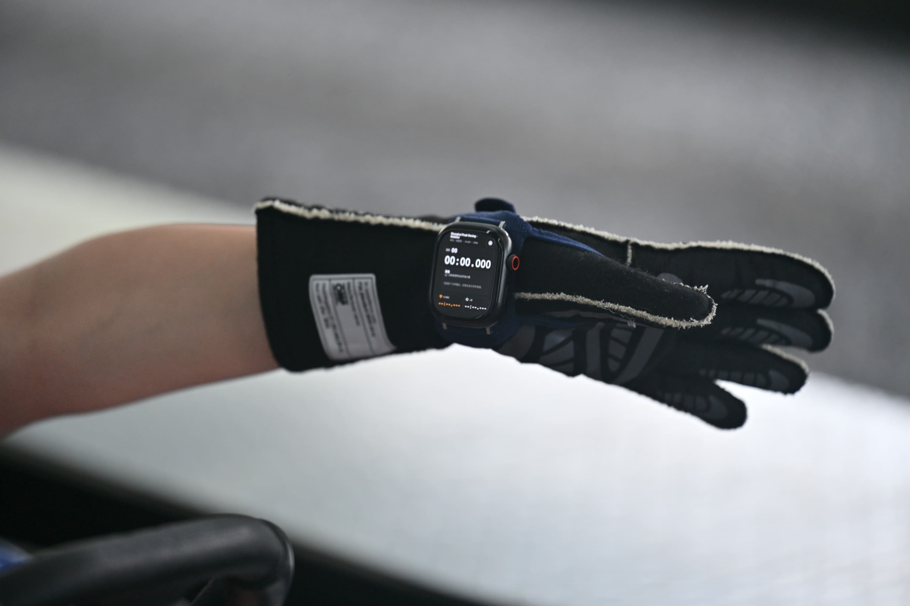 佩戴在赛车手套上的 Dexian 智能手表，屏幕显示圈速计时 / Dexian smartwatch strapped over a racing glove, screen showing lap timing